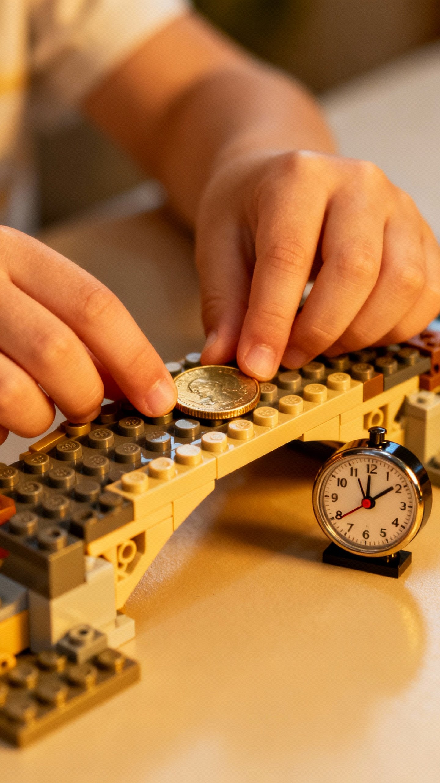 Child’s hands building a Lego coin-holding bridge, timer ticking beside