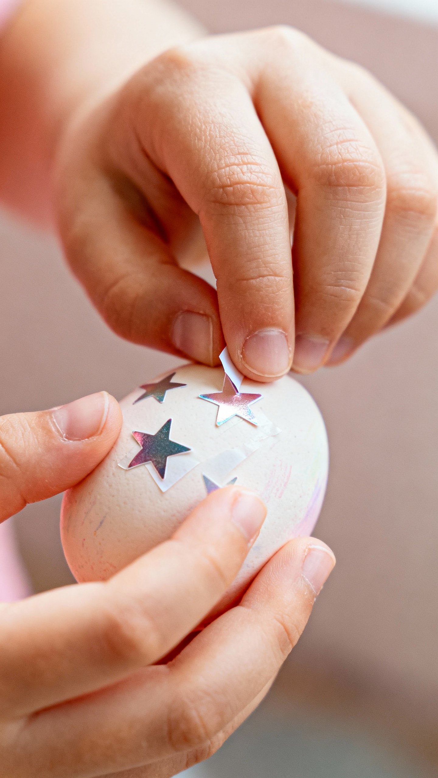 Closeup of child hands peeling star stickers off painted egg